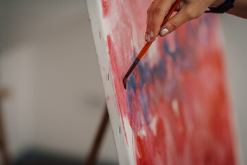 Artist painting colorful abstract artwork on canvas with brush