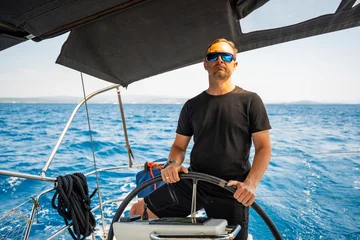 Fototapete Segeln Man standing at the helm of a sailing yacht near Croatia, steering the boat through open water. Leadership, control, sailing lifestyle and freedom at sea.  © dtatiana