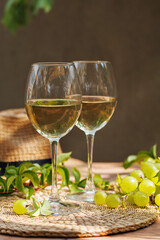 White wine glasses and grapevine leaves on wooden surface with straw hat and natural sunlight..