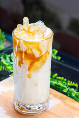 Chilled coconut milk drink with sweet corn and syrup drizzle, served with ice in a clear glass on a wooden surface and green background.