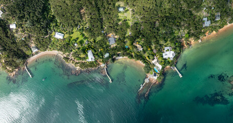 Aerial view of coastal homes nestled amongst lush greenery along the shoreline of Kawau Island, New...