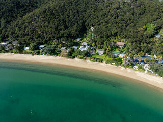 Aerial view of beach houses nestled between lush forest and turquoise water. This is a coastal...