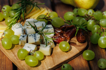 Blue cheese, sliced cheese, grapes, and dates on wooden board served as summer snack..
