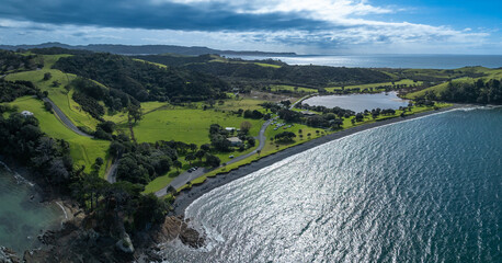 Aerial view of a black sand beach and green hills in Tawharanui Regional Park, New Zealand. The...