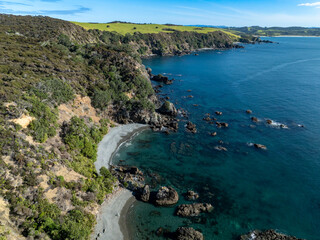 Aerial view of a rugged coastline with lush green hills meeting the turquoise waters of the Pacific...