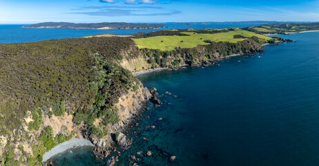 Aerial view of the coastline in New Zealand. The image shows the rugged cliffs, lush green hills,...