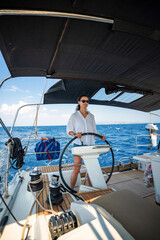 Young woman steering a sailing yacht near Croatia, confidently standing at the helm. Female...