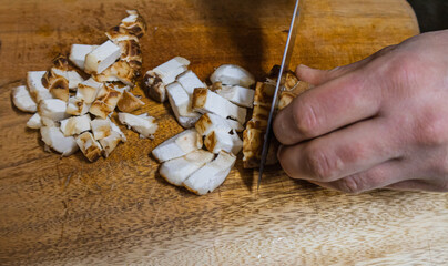 man cutting shiitake mushrooms into cubes with knife on wooden board in restaurant, close up