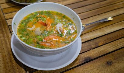 Thai traditional tom yum soup with shrimp, octopus and squid in bowl on wooden table background