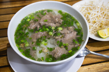 Vietnamese traditional cuisine, beef pho bo soup with greens, rice noodles, ginger, lime, cilantro and chili pepper in a bowl. Po-bo soup\pho bo soup