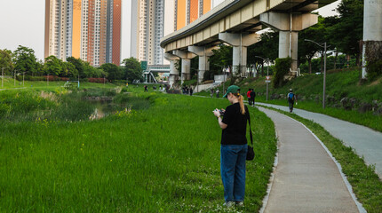 girl in the park controls a drone. A pretty woman of European appearance in a cap and jeans holds a remote control for a quadcopter. Long shot, full-length