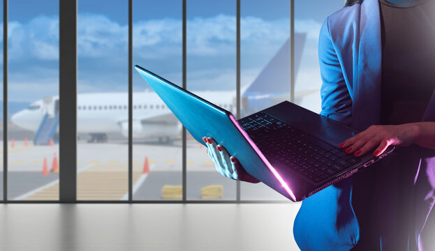 Laptop in hands of businesswoman. Woman at airport. Businesswoman waiting for plane. Lady in formal wear holding computer. Manager holding open laptop. Staff standing in airport terminal