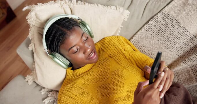 Black woman, headphones and singing with phone on sofa, above and scroll on social media at home. African girl, smartphone and audio tech with mobile app, chat and streaming subscription at apartment