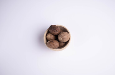 whole nutmeg in a wooden bowl on a white background