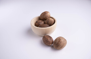 whole nutmeg in a wooden bowl on a white background