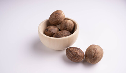 whole nutmeg in a wooden bowl on a white background