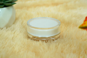 close up of a white cream jar stands on a yellow fur. use for product mockup display