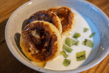Syrniki, Eastern European cheese pancakes, served with yogurt and kiwi. A comforting, rustic dish, blending savory cheese with sweet tangy fruit.