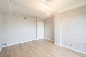 Empty room with light wood floors, textured walls, white trim, and a single bare bulb hanging from the ceiling. Minimalist