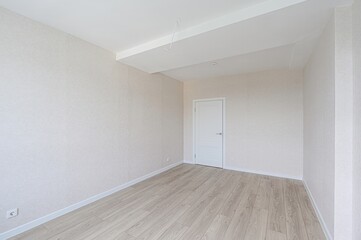 bright, empty room with light beige wallpaper, wood flooring, a white door, and a white ceiling