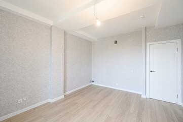 Empty room with light wood floors, textured walls, white trim, and a single bare bulb hanging from the ceiling. Minimalist