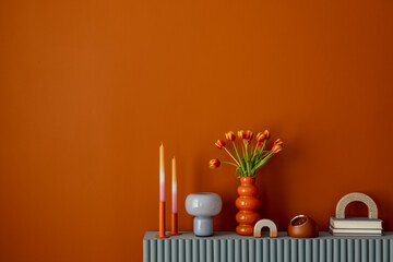 Contemporary decor with tulips in an orange vase, pastel candle holders and sculptural accents on a fluted blue console. Copy space.