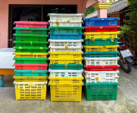 A medium shot captures three vertical stacks of colorful, weathered plastic crates. The crates are arranged in a repeating pattern of white, red, yellow, and green, suggesting their use for a market