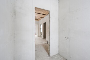 bright, unfinished room. White walls lead to a doorway. Inside, more bare rooms. Construction is ongoing