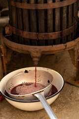 Traditional winemaking process featuring a wooden wine press extracting rich red juice into a metal...