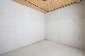 corner in a room under construction. The walls are plastered, the floor is concrete, and the...