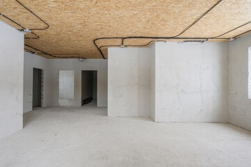 An unfinished room with bare walls, a plywood ceiling and exposed black electrical wiring. There are several doorways leading to other rooms