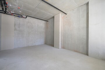 unfinished room with bare concrete walls, floor, and ceiling. Black pipes run along the ceiling