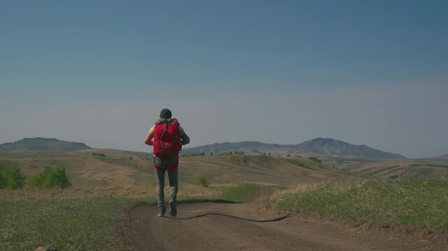 Solo traveller man walks among meadows and hills, preparing for taking off with paraglider. A man with a folded parachute on his shoulders in the wilderness.