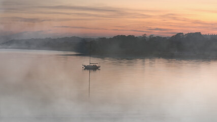 Sailboat Reflected in Calm Misty Estuary at Sunrise 