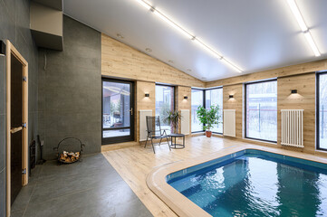 Indoor pool area with a sauna, wood-paneled walls, large windows offering a view of a snowy...