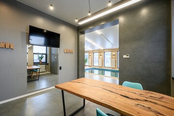 Modern interior with a wooden table, blue chairs, and a view through an opening to a pool area....