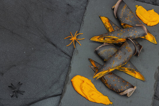 Halloween sweet dessert with traditional decor. Thin black pancakes with pumpkin cream, fall leaves - Powered by Adobe