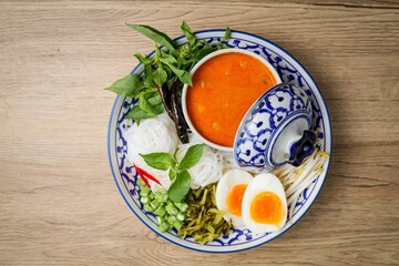 Kanomjeen namya krati ,Rice vermicelli with minced fishes and coconut milk in red curry on ceramic plate side dish with vegetables and boiled egg	