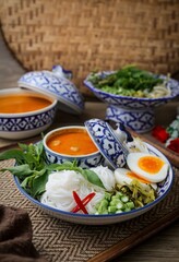 Kanomjeen namya krati ,Rice vermicelli with minced fishes and coconut milk in red curry on ceramic plate side dish with vegetables and boiled egg