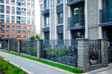 Modern residential complex with brick columns, wrought iron fences and large windows. Cozy courtyard, neat sidewalks, greenery and parking.