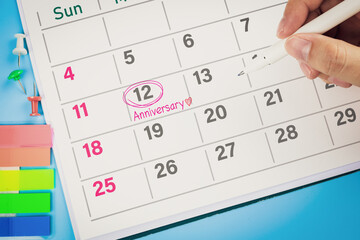 Close-up view of hand using pen to draw pink circle on calendar with write word Anniversary and heart. Concept of wedding anniversaries, company anniversary, and celebrations.