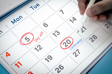 Close-up view of hand using pen to draw red circle on calendar with write word Conference. Concept of appointment reminder, and mission schedule.