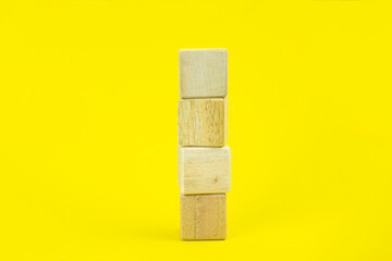 Four empty wooden cubes stacked on a yellow background with copy space. Mockup composition for design.