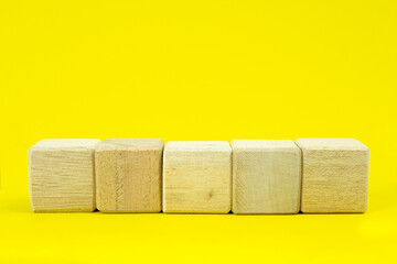 Five blank wooden blocks in a row on a yellow background with blank space for your text, letters or numbers.