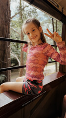 Smiling girl enjoying a scenic train ride through the forest, flashing a peace sign. Puffing Billy adventure, Melbourne, Australia, a joyful moment of childhood summer activities