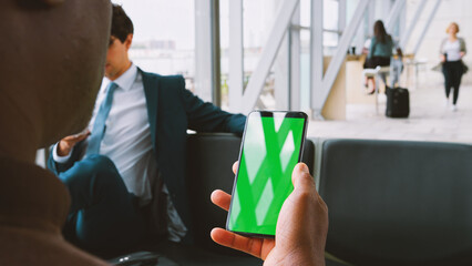 Close Up Of Male Passenger In Airport Departure Lounge Looking At Green Screen On Smart Phone