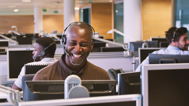 Mature Businessman Wearing Telephone Headset Working In Customer Services Department