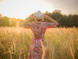 Young woman walking through picturesque European field in late summer. Golden sunlight, lush greenery, and serene rural atmosphere create peaceful countryside scene.