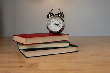 Classic alarm clock resting on books with ambient warm lighting in a peaceful indoor setting.