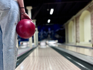 Young woman holds a bowling ball against the colorful backdrop of a dimly lit bowling alley, ready...